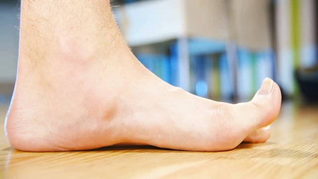 Flat feet toe yoga exercise side view 4K. Low angle view of person's feet in focus while lifting toes. Home dining room in the background out of focus.