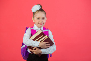 beautiful little girl with a bow with a school satchel on a pink background with a book in hands