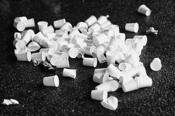 Pile of used disposable white cardboard cups for water on asphalt, concept of ecologic garbage, recycling. Black and white background