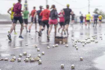 Service point on marathon, group of runners. Used disposable cardboard cups for water on asphalt, blurred, selectiv focus. Sport lifestyle concept
