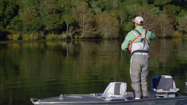 Fisherman fly fishing for trout from a boat in Lake Whakamaru in slow motion.