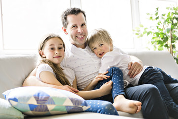 Fototapeta premium Father and his nine years kid girl and 5 years boy on the sofa at home