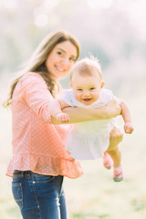 Fototapeta premium Young mother holding daughter in her arms. Beautiful Mother And Baby outdoors. Nature. Beauty Mum and her Child playing in Park together. Outdoor Portrait of happy family. Joy. Mom and Baby