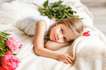 Cute little girl with peonies in studio lying on the bed among peonies