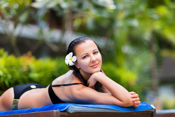 Young woman gets suntan near tropical swimming pool in bikini