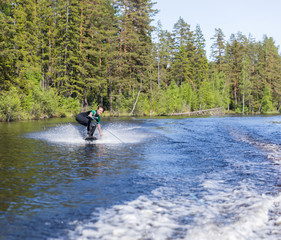 Young pretty slim brunette woman in wetsuit riding wakeboard on