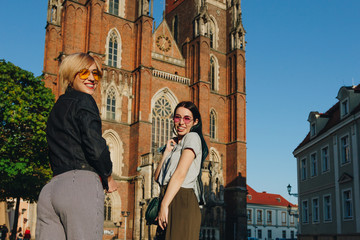Fototapeta premium two attractive smiling women standing in front of wroclaw cathedral and looking at camera
