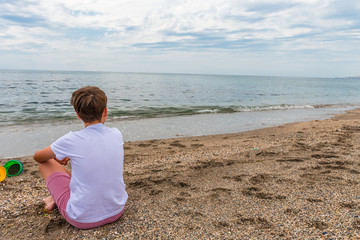 Fototapeta na wymiar Child sitting on the sand near the seashore contemplating the horizon