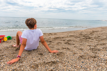 Child sitting on the sand near the seashore contemplating the horizon