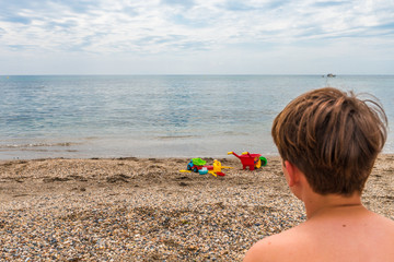 Child sitting on the sand near the seashore contemplating the horizon on a cloudy day