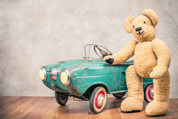 Teddy Bear standing near rusty outdated retro turquoise toy pedal car in front concrete textured wall background. Vintage style filtered photo