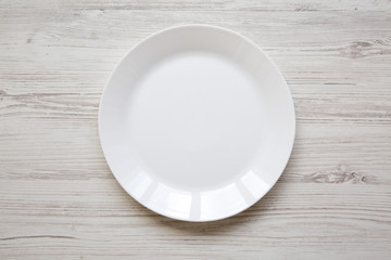 White plate on white wooden background, top view.