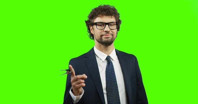 Portrait of the attractive succesful man in the glasses, suit and tie posing in front of the camera and spinning keys on his finger. Green screen. Chroma key.