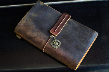 Travel note on black background. Handmade paper diary notebook in brown leather cover. Old vintage leather book, top view.