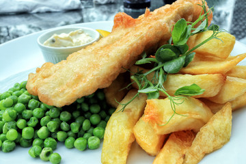 Crispy battered fish and chunky potato chips served with boiled green peas and mayonnaise, traditional English food .