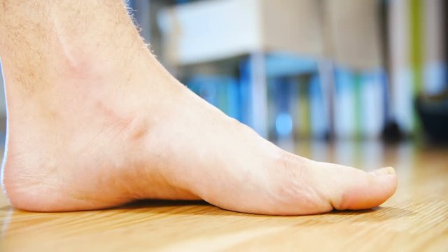 Flat feet forcing arch up exercise close-up 4K. Low angle view of person's foot in focus while lifting arch to make a healthy foot. Home dining room in the background out of focus.