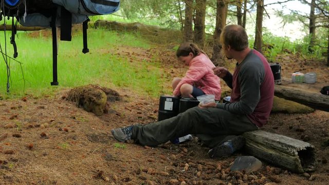 Father sits next to daughter while camping, to snack on food and talk.