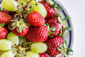 Close up of a bowl of juicy and ripe fruit, strawberries and grapes. vintage background, shallow depth in focus. Concept rustic nostalgia.