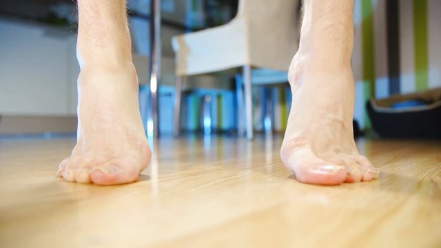 Stand on toes heel rise training flat feet arch 4K. Low angle view of person's feet in focus while lifting on toes. Home dining room in the background out of focus.
