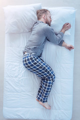 Recharging my batteries. Top view on a young man wearing pajamas taking a nap and sleeping tight after getting tired at home.