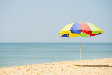 A colorful umbrella is open on a tropical beach during a sunny day.