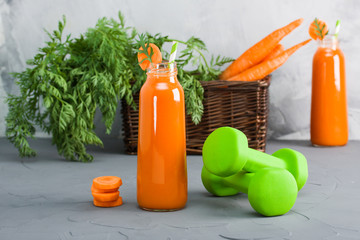 Two bottles with fresh carrot juice and green dumbbells