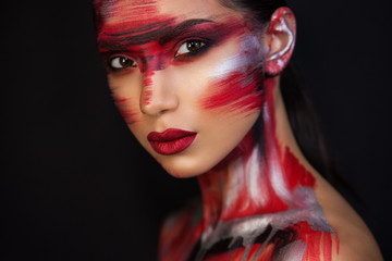 the Euro-Asian woman looks directly at us, on a black background, sensual red lips are closed, red silver black makeup emphasizes her image