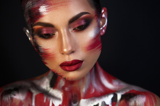 the Euro-Asian woman looks down, the red lips on a black background are well underline the image, a metallic red makeup.
