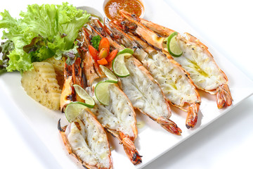 Grilled Cut-off black tiger shrimps with boiled potatoes, slice of limes, fresh vegetables and chili sauce on white square plate, isolated on white background, Close-up macro high angle top view.