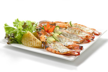 Roasted sliced black tiger shrimps with baked potatoes, slice of limes, fresh vegetables and chilli sauce on white square plate, isolated on white background with shadow, low angle front side view.