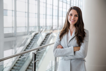 Cheerful successful businesswoman portrait in large financial bank building with arms folded