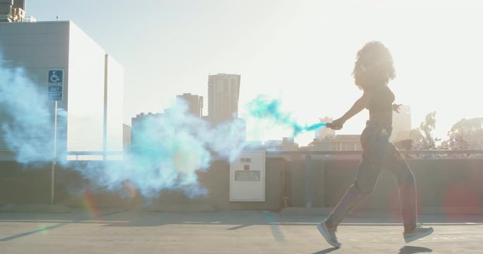 Young woman dancing on rooftop with smoke grenade