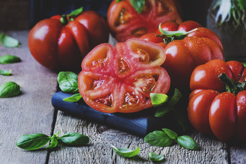 Big red tomatoes with green basil leaves on the old wooden background, selective focus