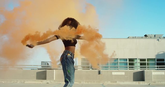 Young woman dancing outside with smoke grenade at sunset on rooftop parking garage 