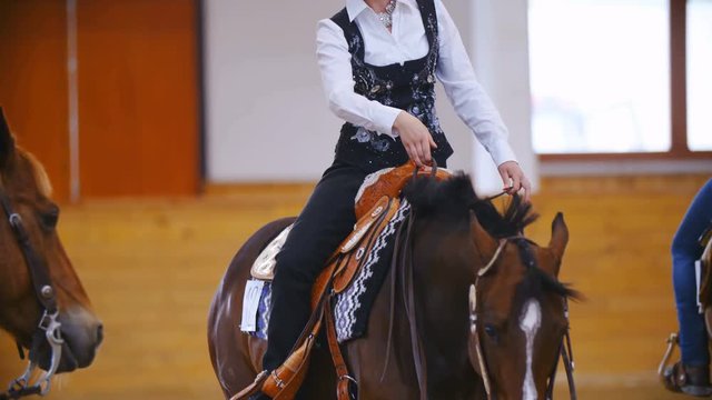 Elegant horse rider single-handed steering the horse in slow motion . Long shot of headless elegant cowgirl in focus gently riding western horse. Black and white dress style.