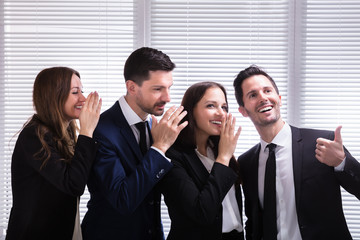 Businesspeople Whispering Into Male Colleague's Ear