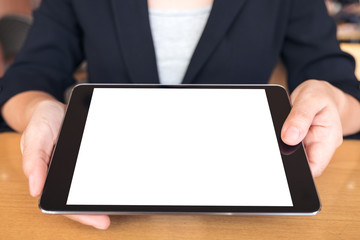 Mockup image of businesswoman holding and showing a black tablet pc with blank white desktop screen on table