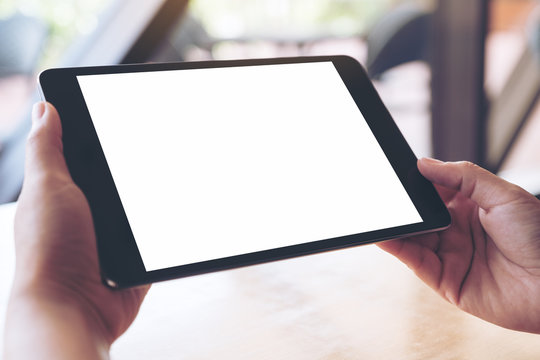 Mockup image of hands holding and using a black tablet pc with blank white desktop screen
