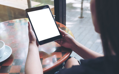 Mockup image of a woman holding black tablet pc with white blank screen and coffee cup on table background