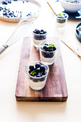 Fototapeta na wymiar Vanilla pannacotta inside small cup and fresh blueberries. frontal view with golden spoon, and other tools