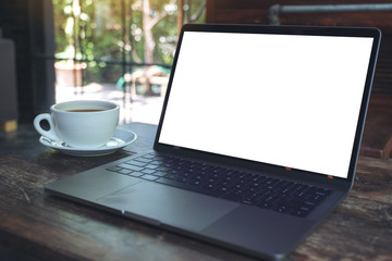 Mockup image of laptop with blank white desktop screen and coffee cup on wooden table in modern cafe