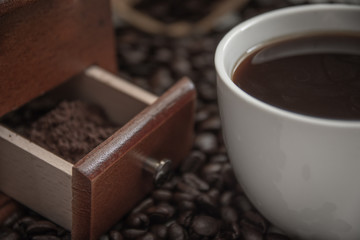 Coffee cup and coffee beans on table with powder in coffee grinder.