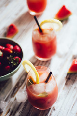 Watermelon and strawberries fruit juice on glass with mint leaves on a white board, flare from backlight.
