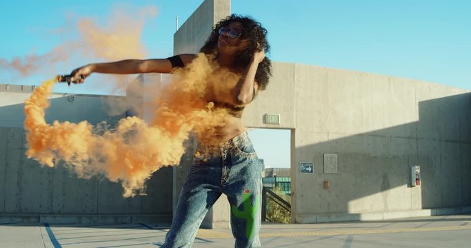 Young woman dancing outside with smoke grenade at sunset on rooftop parking garage 