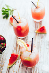 Watermelon and strawberries fruit juice on glass with mint leaves on a white board, flare from backlight.
