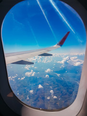 Looking thru airplane 's window seeing wing of airplane , white clouds and blue sky