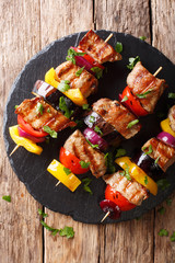 Juicy grilled kebabs of pork with tomatoes, pepper, onions and eggplants close-up on a table. Vertical top view from above