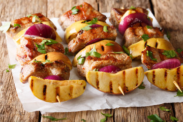Rustic juicy kebabs of pork with apples and red onions close-up on parchment. horizontal