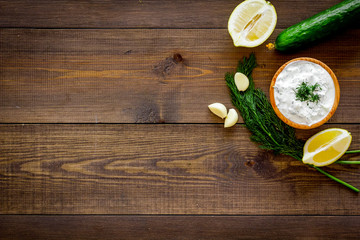 Fototapeta na wymiar Greek yogurt dip with greenery, cucumber, oranges, garlic on dark wooden background top view space for text