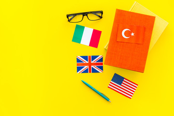 Language study concept. Textbooks or dictionaries of foreign language near flags on yellow...